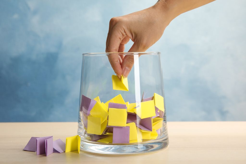 a hand picking a small piece of paper out of a glass jar